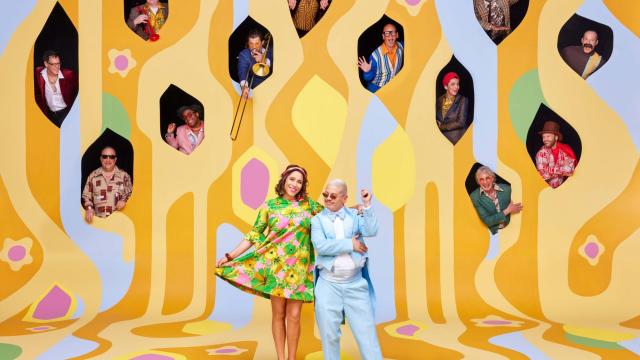 two people standing in front of a yellow background with lots of holes cut out and people sticking their heads out of the holes