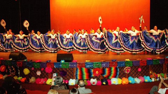 A line of Ballet Folklorico dancers in blue skirts with colorful trim.