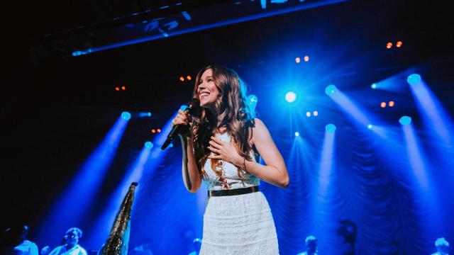 Joss Stone in white dress with blue stage light beaming behind her