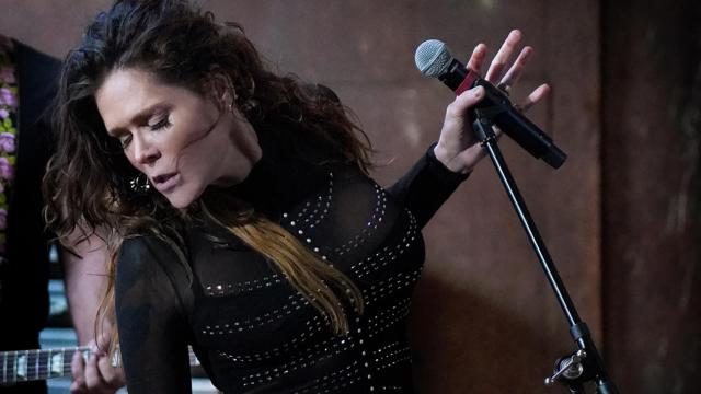 woman standing at a microphone wearing all black and looking away