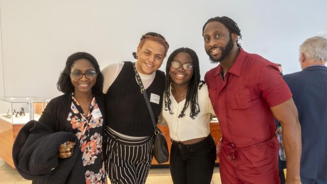 Four people pose, arm in arm, smiling at the camera