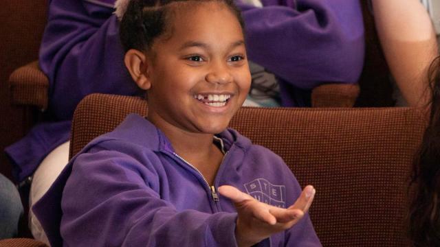 Two young girls sit in theatre seats, enjoying a show
