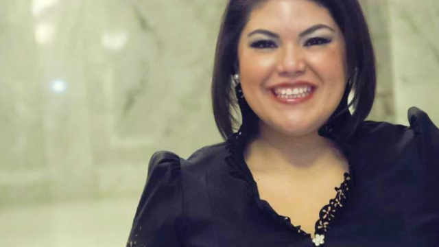 A woman in a black blouse and silver earrings smiles at the camera.
