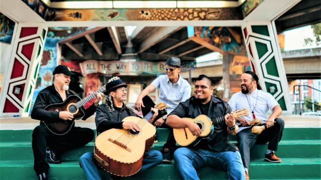 five men with instruments sitting on steps, smiling and looking at each other