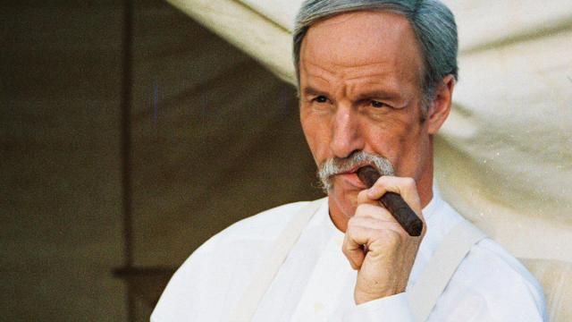 Wyatt Earp smokes a cigar while reclining in a tent.