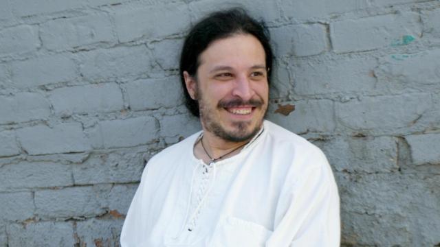 Leon Santiago, wearing a white shirt and white pants, leans back against a white brick wall.