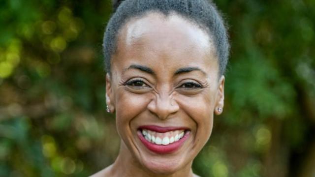A woman smiles brightly at the camera, her hair pulled back in a ponytail