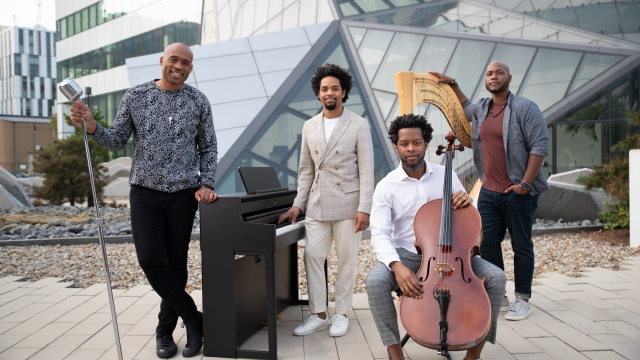 Four artists stand with their string instruments in front of a modern building