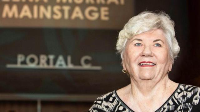 A woman with silver hair and blue eyes smiles in front of Portal C at the theatre