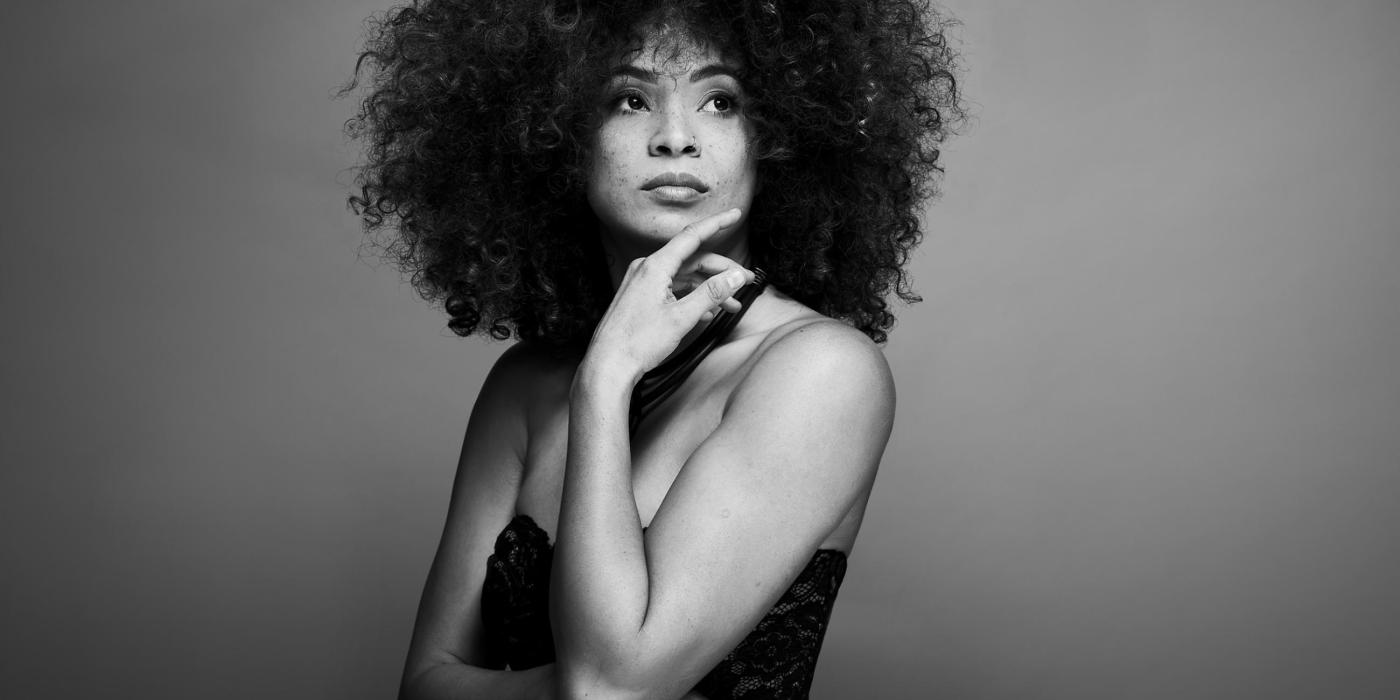 Kandace Springs poses with her hand under her chin, wearing a black dress