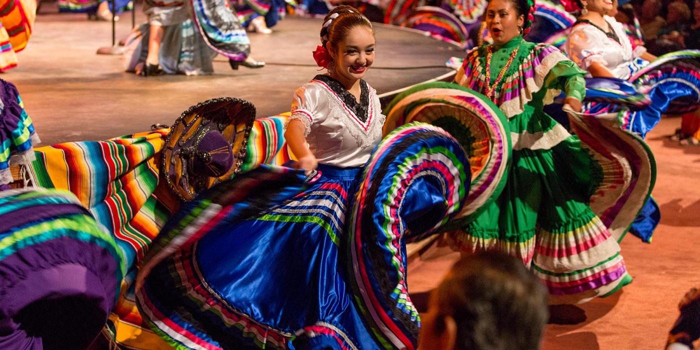 Brightly dressed dancers flourish their traditional Mexican dance skirts in front of a stage