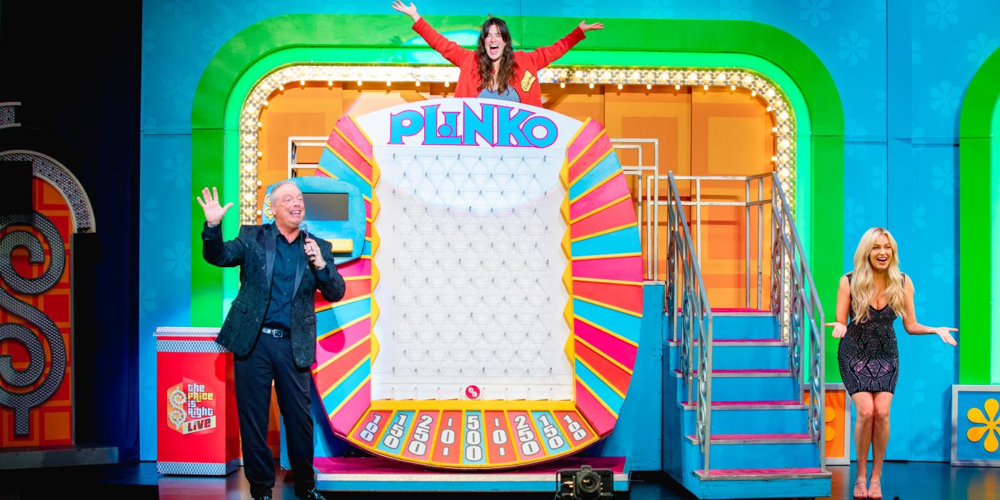 three excited people on stage surrounding a giant plinko game
