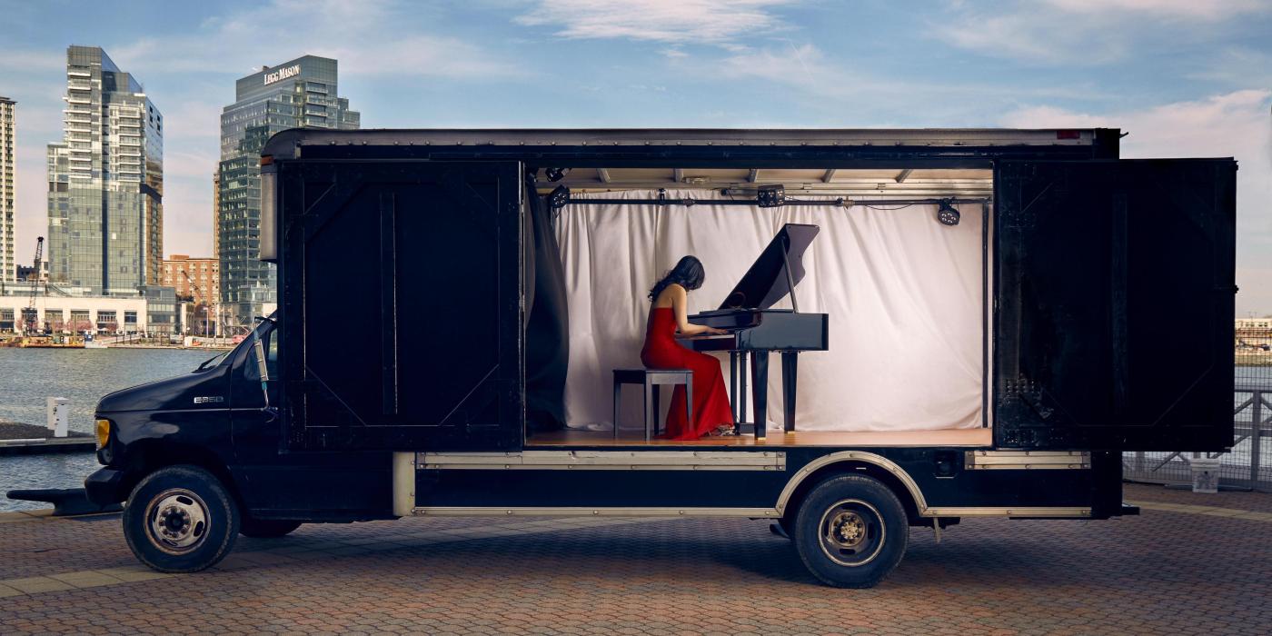 pianist in red dress playing piano inside of a truck