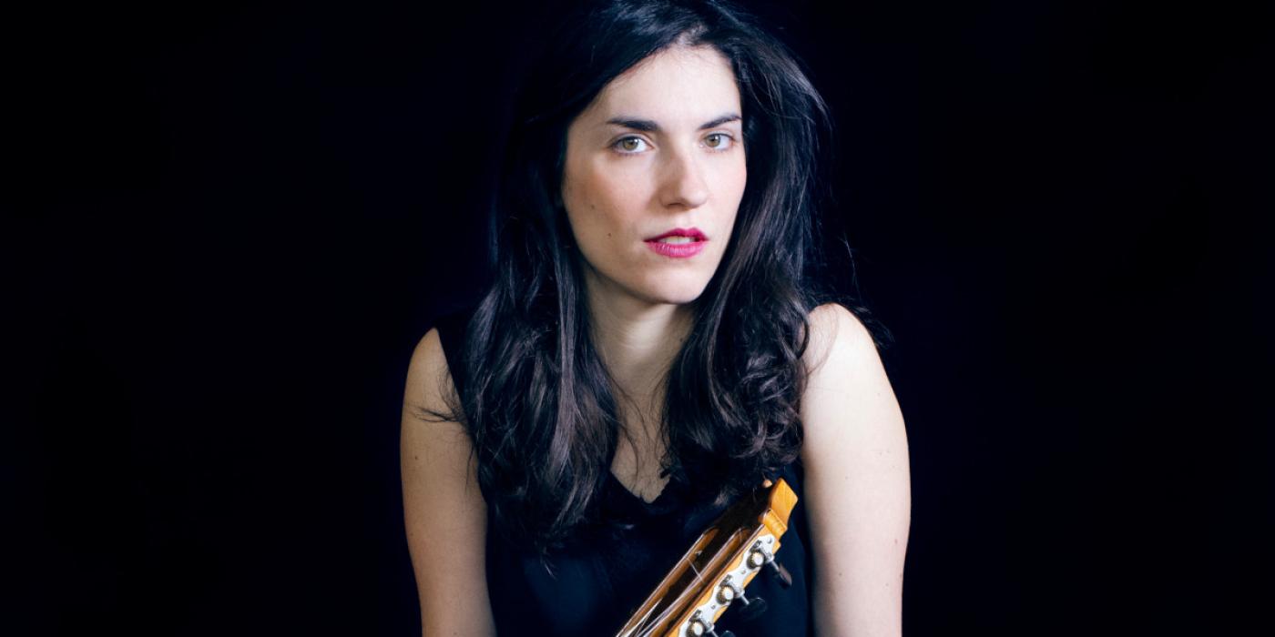Caucasian woman wearing a black dress with a brown acoustic propped next to her. 