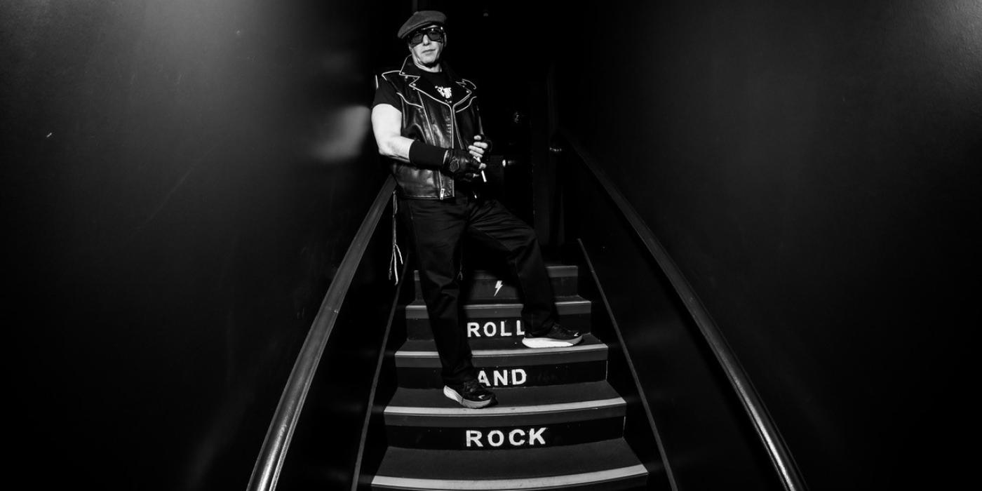 Andrew Dice Clay stands on a dark stairwell