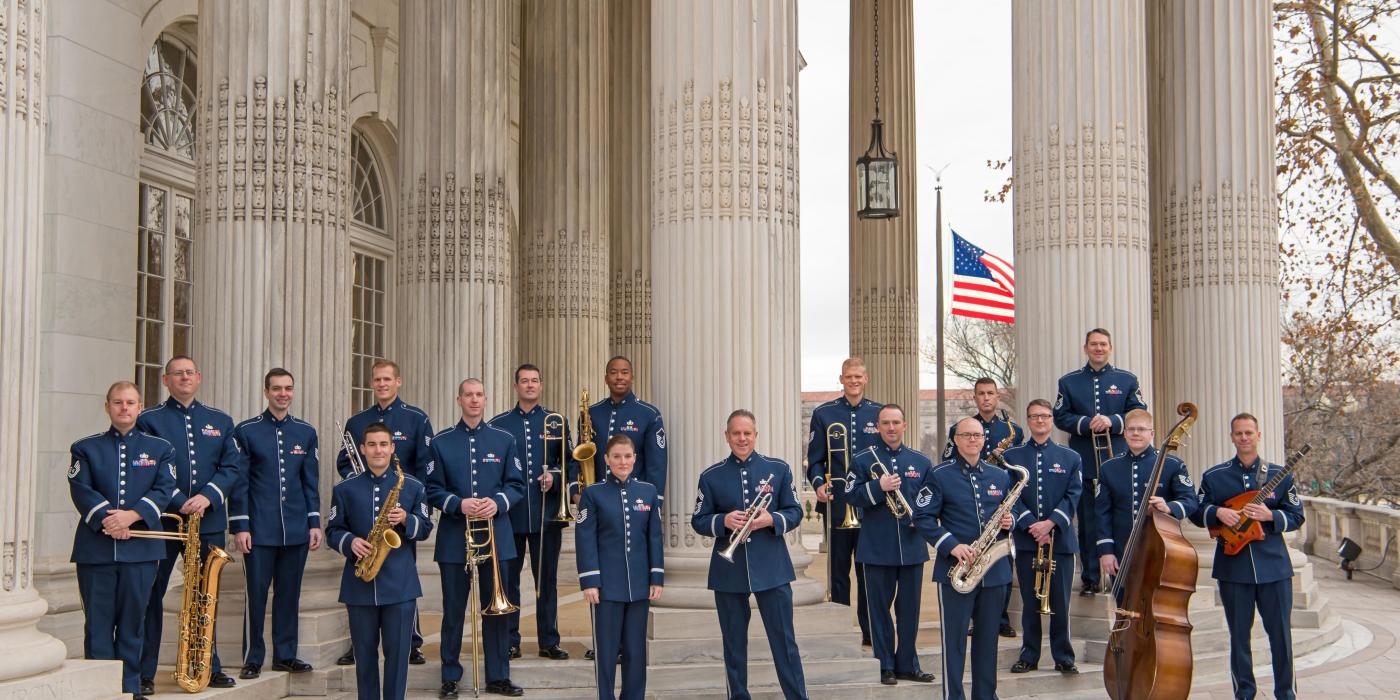 18 men in dress blues pose with their instruments