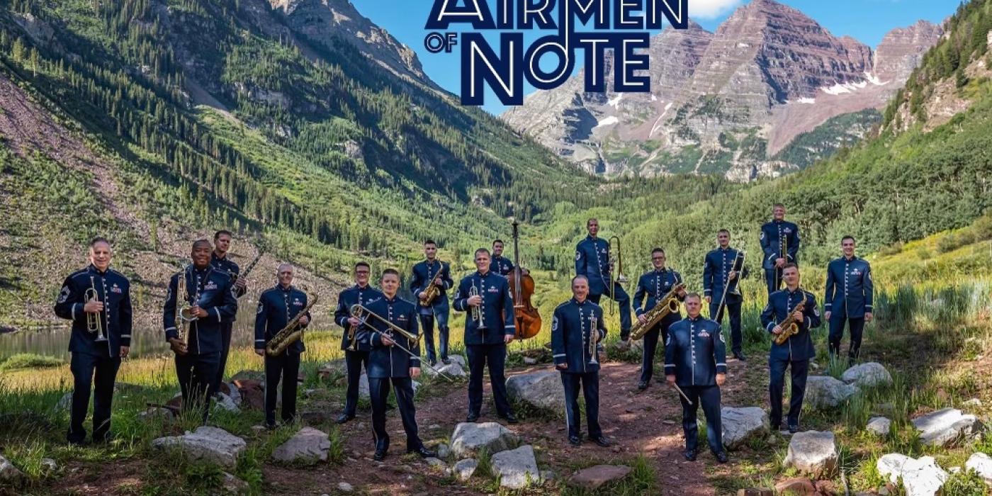 United States Air Force Band Airmen of Note standing at the base of a mountain, in uniform holding their instruments