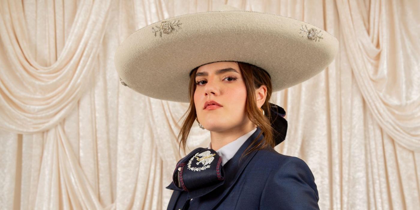 Woman posing in navy blue traje de charro outfit with a cream colored hat