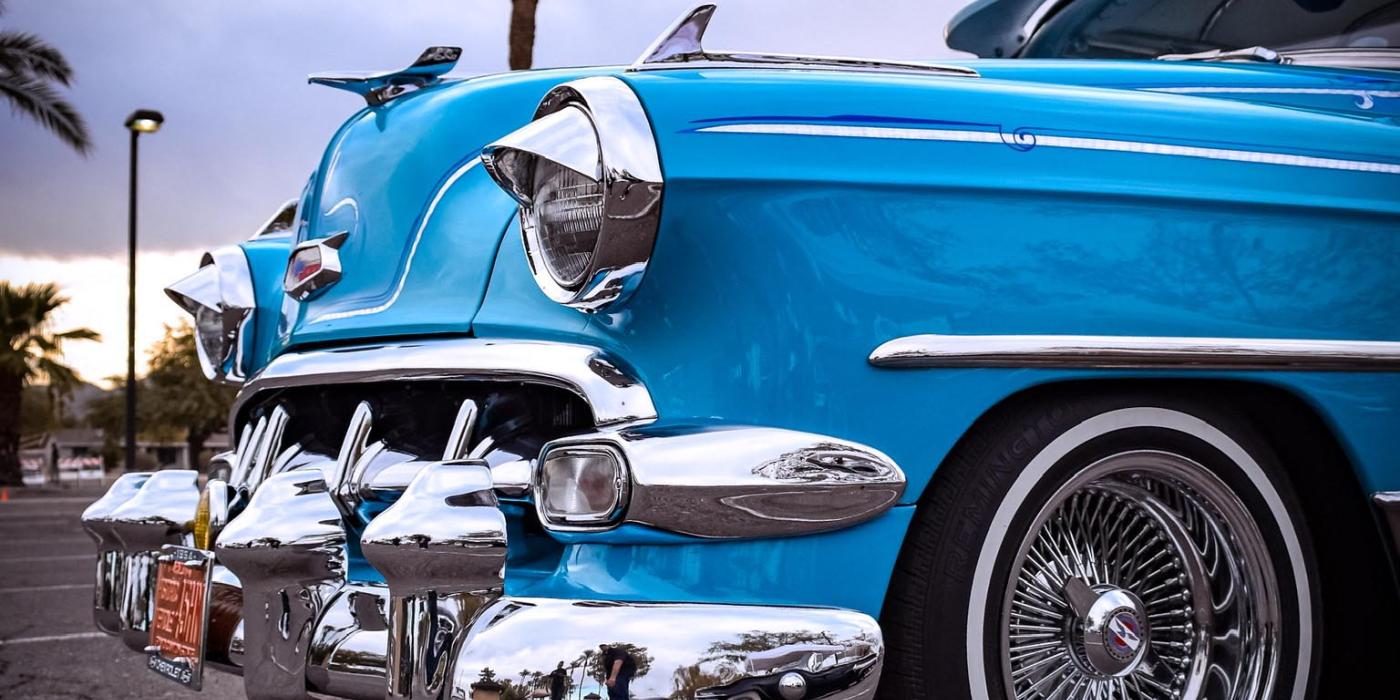 The photo shows a vintage blue car with a chrome bumper and white wall tires