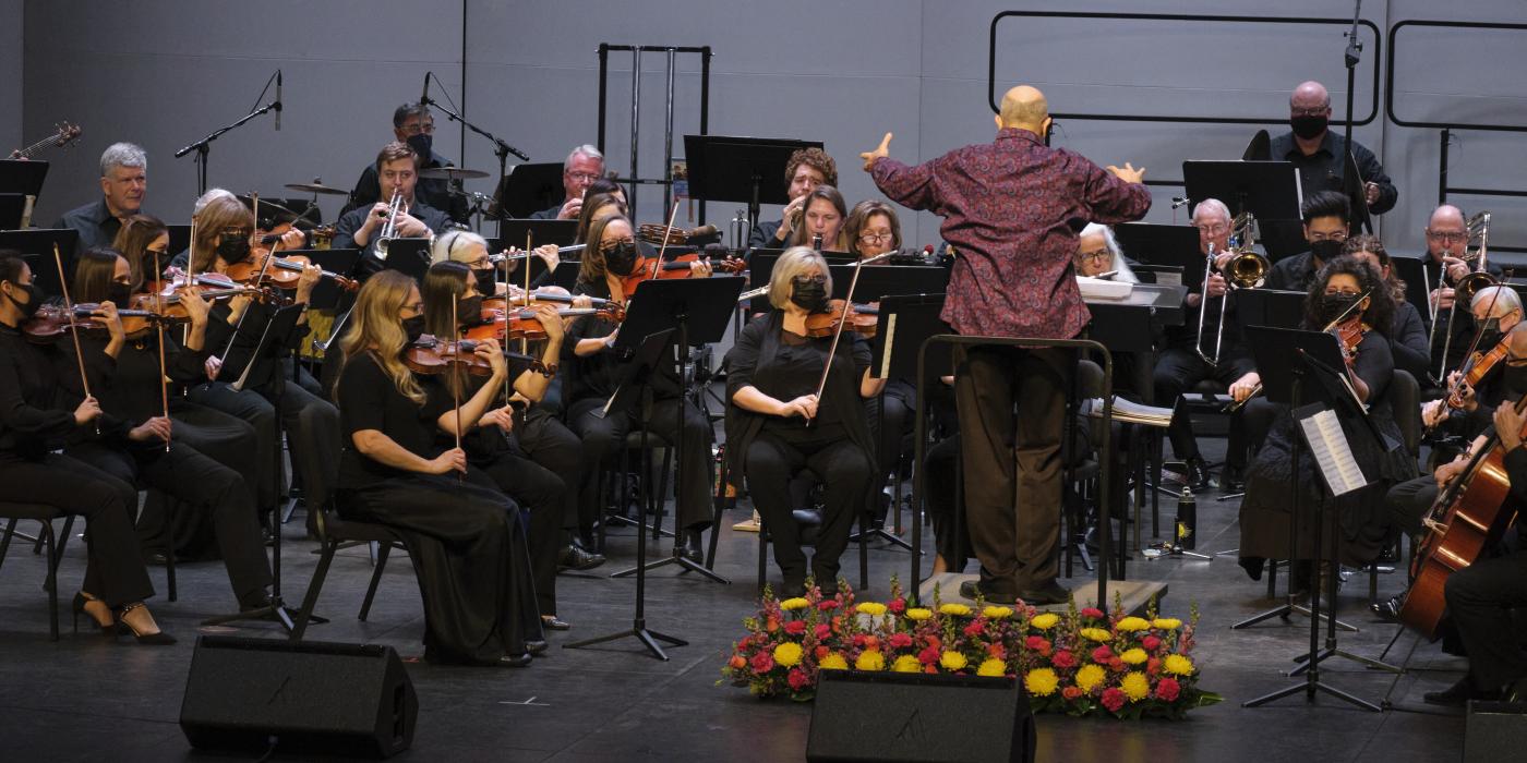 An orchestra plays on a stage with the conductor in front of them. 