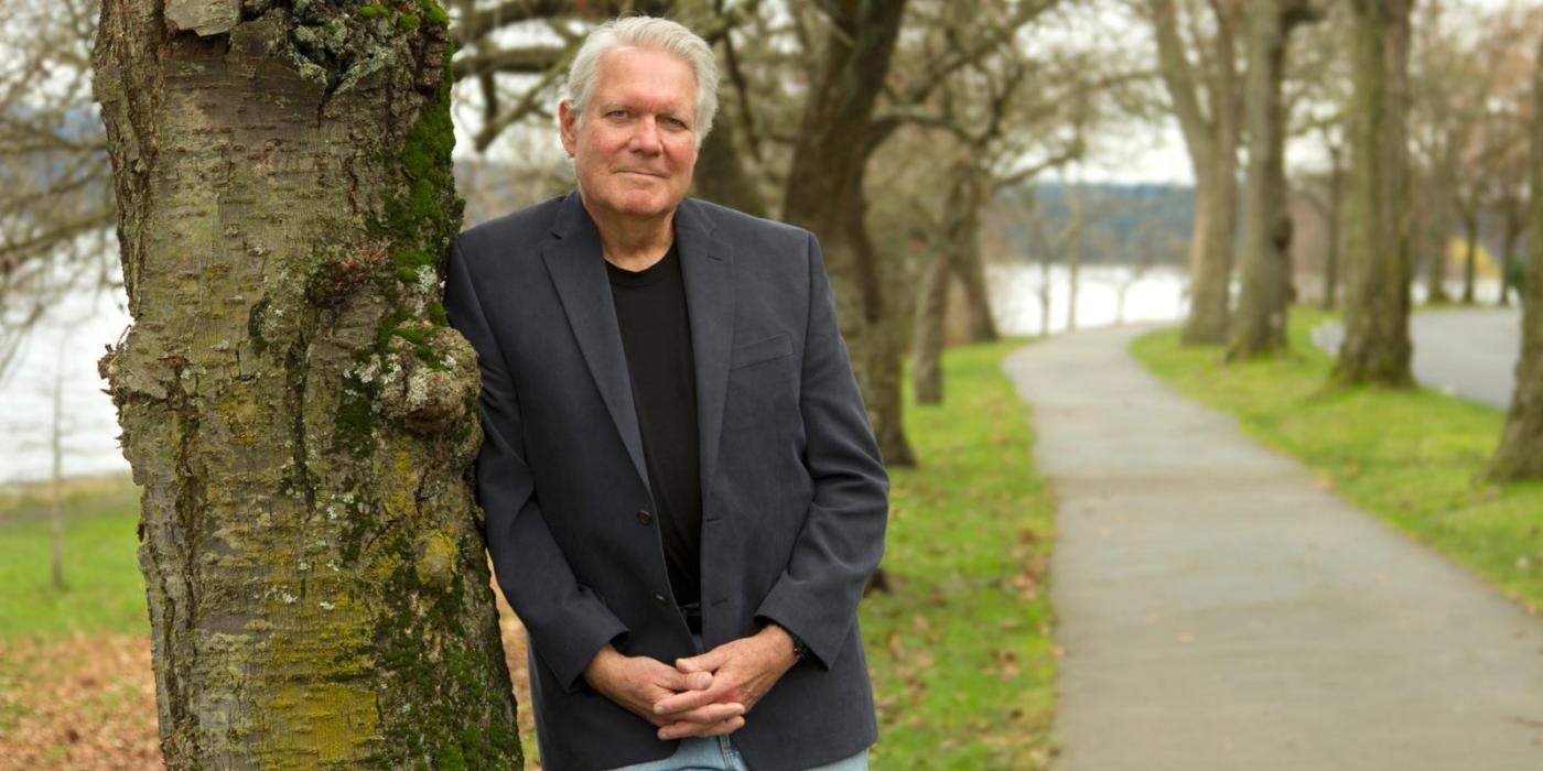 Paul Green poses outdoors, leaning on a tree.