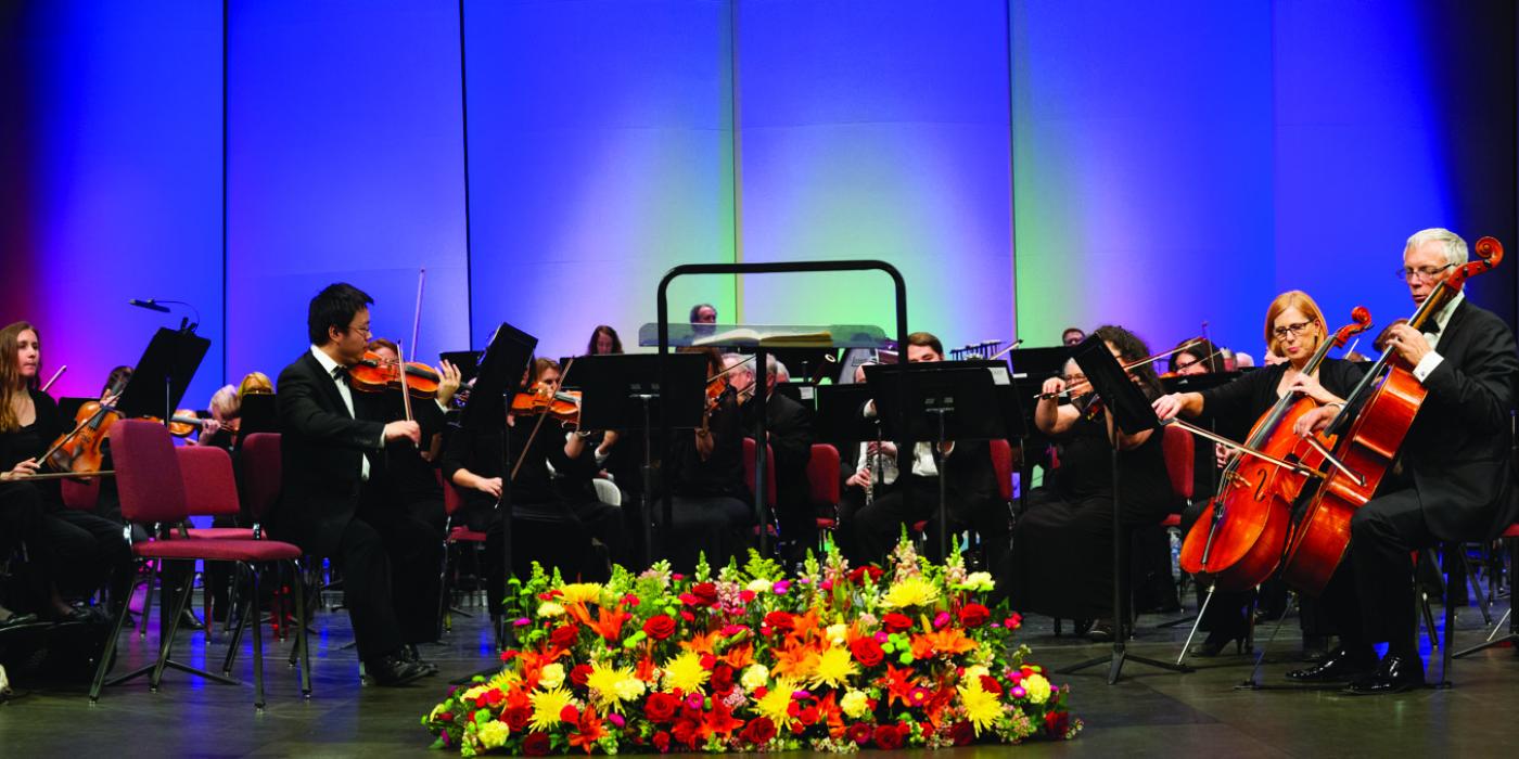 An orchestra sits assembled on the stage with a blue background