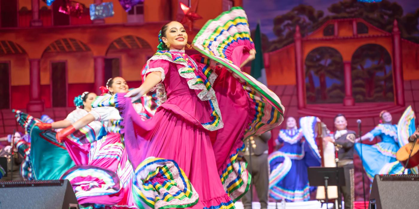 A folklorico dancer in a bright pink dress dances with her skirts fluttering around her