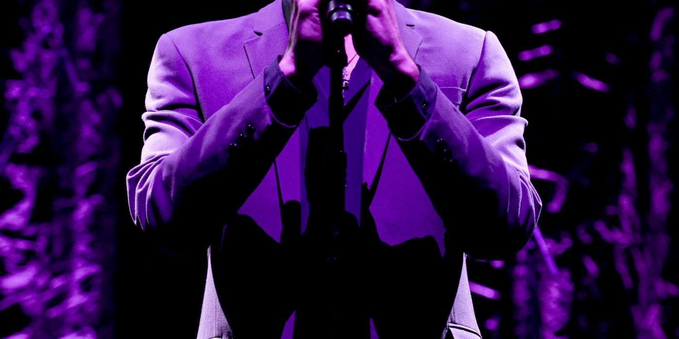 On stage wearing a purple jacket and wearing sunglasses