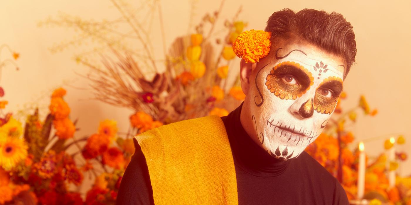 A man with dark hair and a face painted like a skeleton looks at the camera