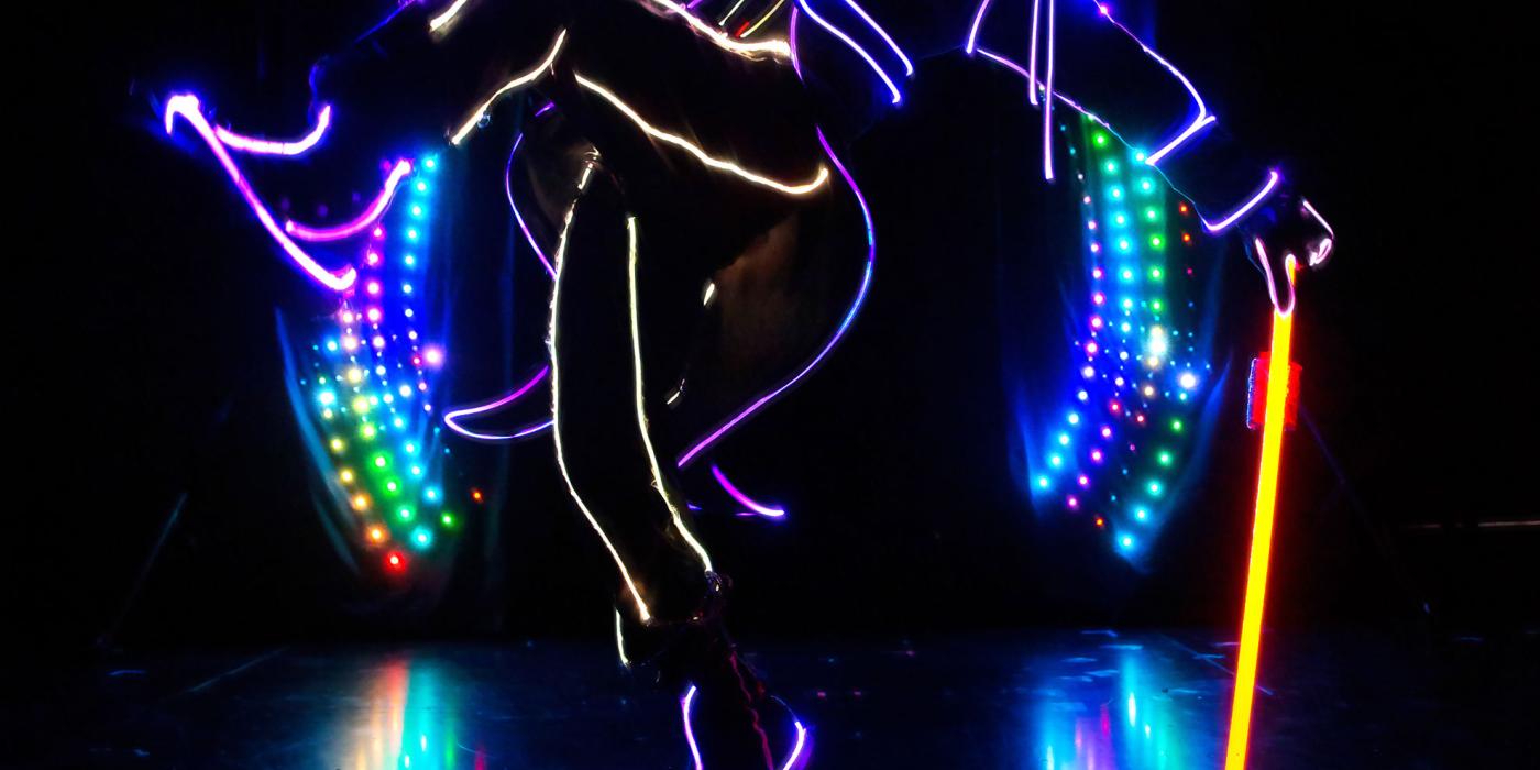 iLuminate performer on a dark stage lit and outlined as man with a top hat, suit and cane