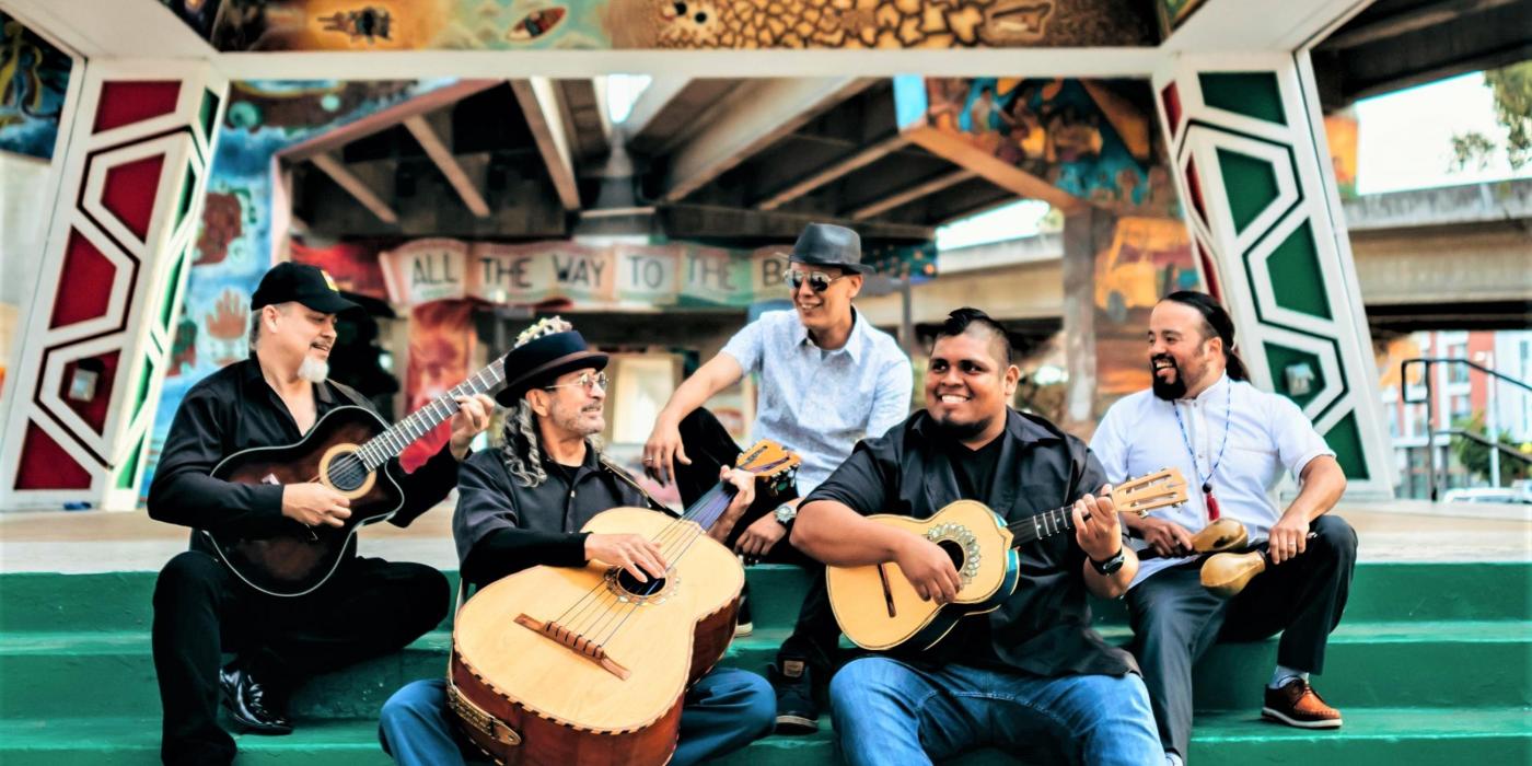 Five men sit on green stairs, some of them holding string instruments.