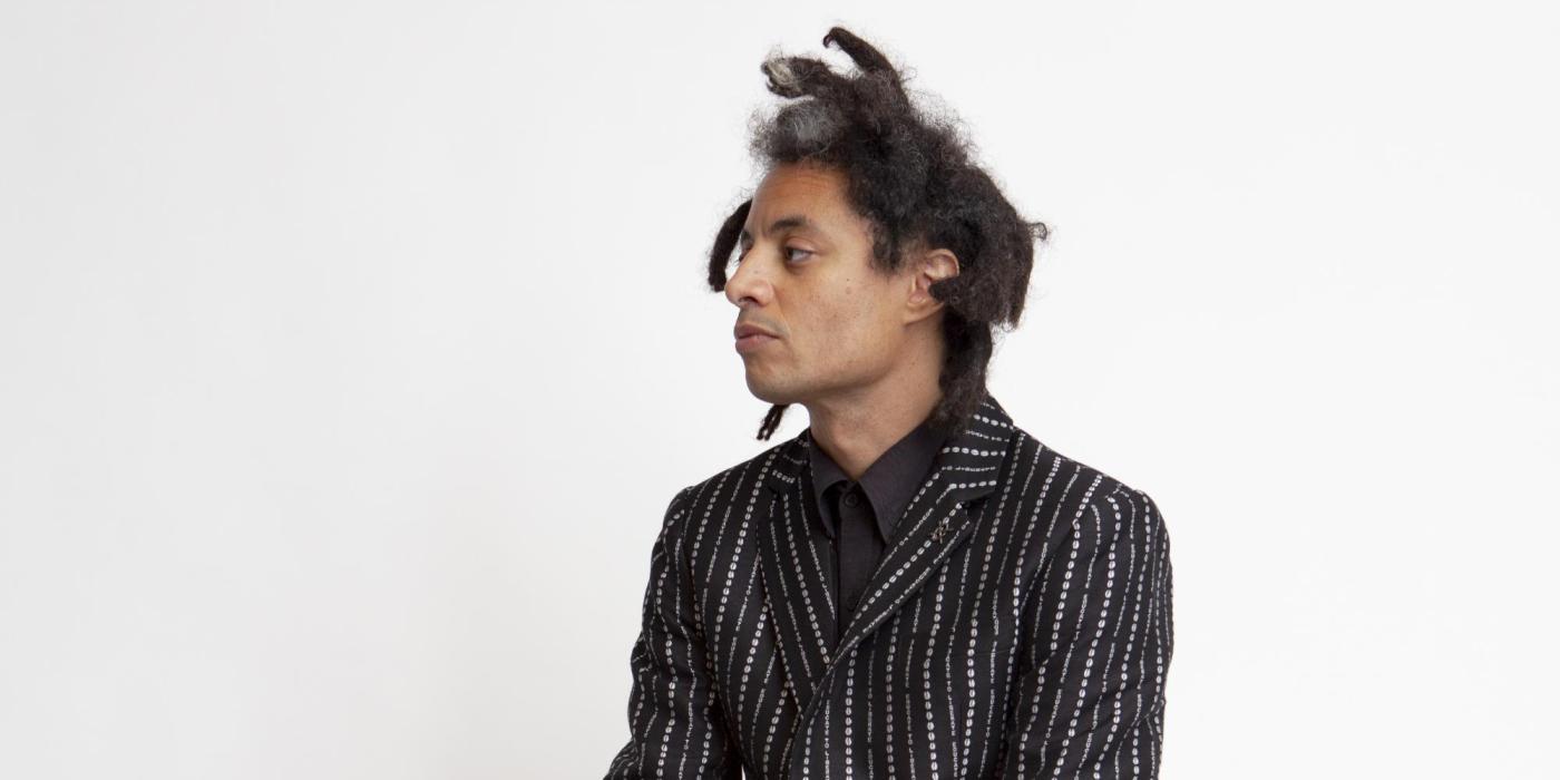 Black man with dreadlocks sitting on a box in a black suite with white pinstripes