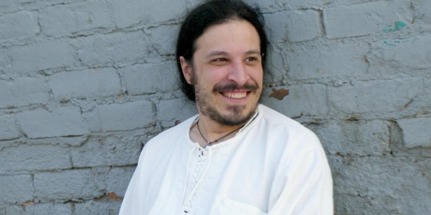 Leon Santiago, wearing a white shirt and white pants, leans back against a white brick wall.