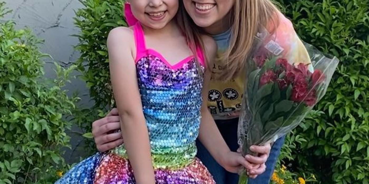 A blond woman poses with a young dancer dressed in a rainbow colored dress