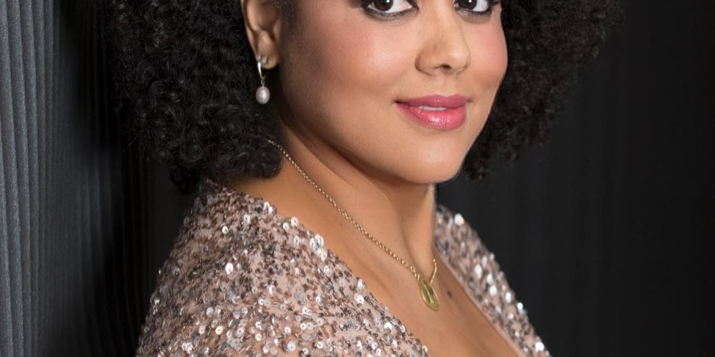 Kim Nalley wearing a gold sequence dress with a white flower in her hair