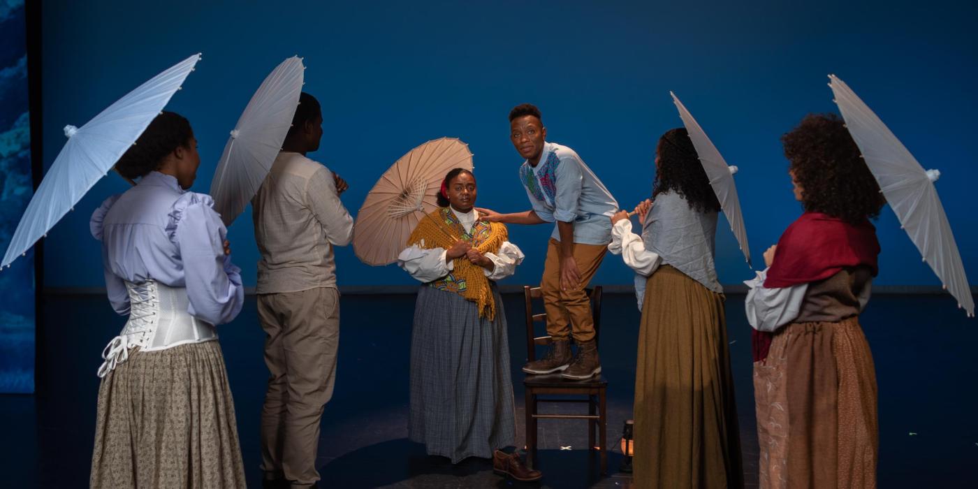 Five women with umbrellas listen to a young man tell his story