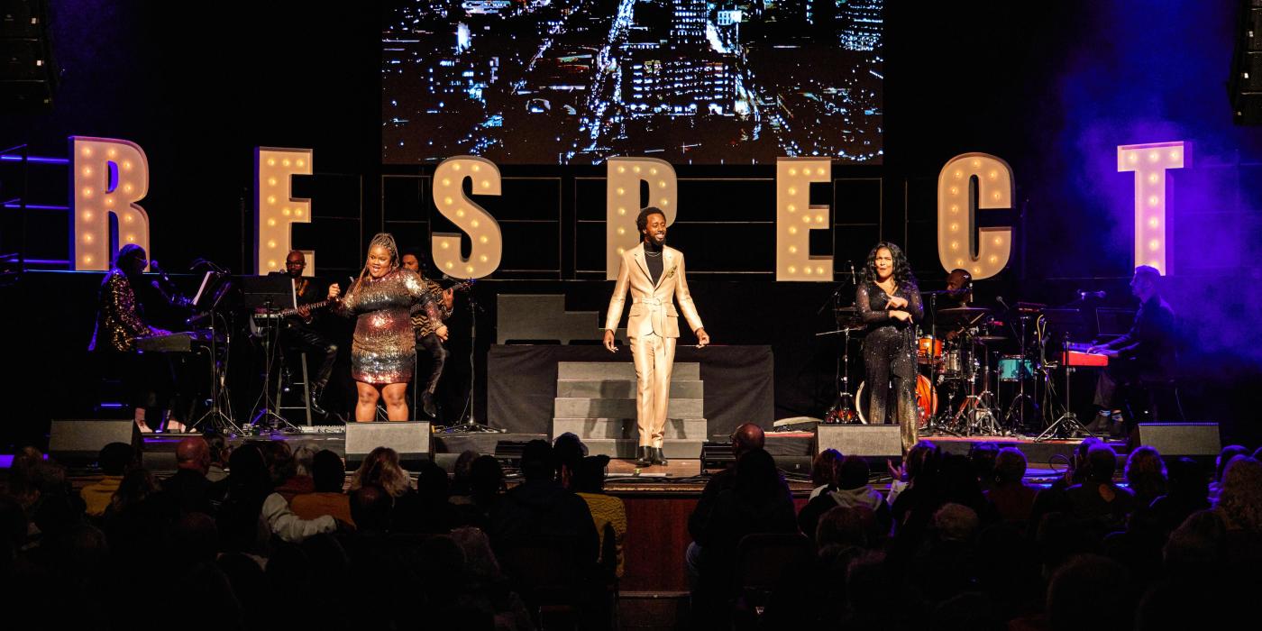 three singers performing on stage in front of large letters spelling out RESPECT