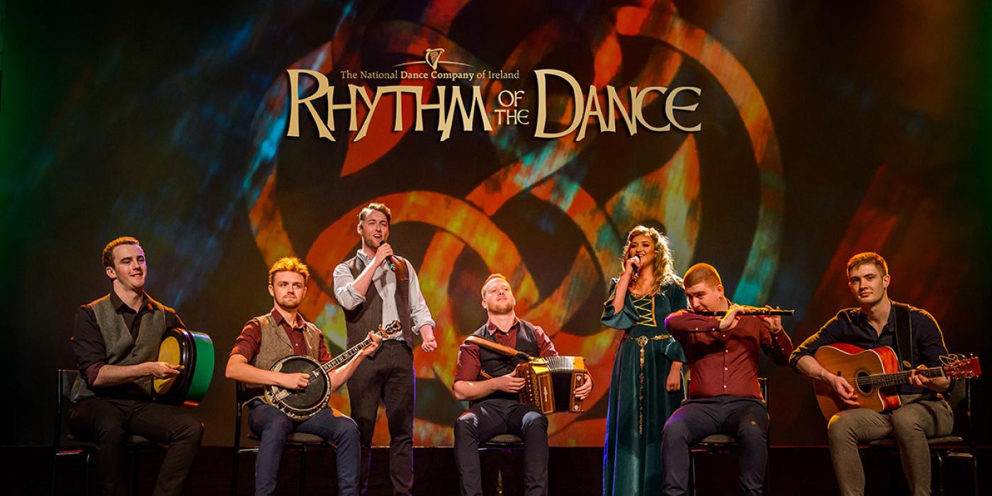 Four men hold traditional folk instruments with two singers - a woman and a man in their midst