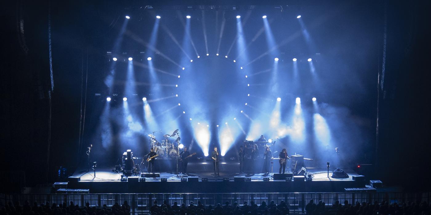 A band performs on a stage with dramatic blue lights streaming around them