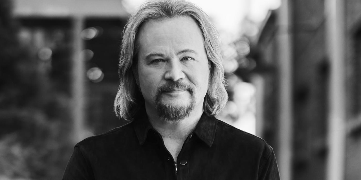 A man with shoulder-length blond hair wears a black cowboy style shirt in a black and white photo