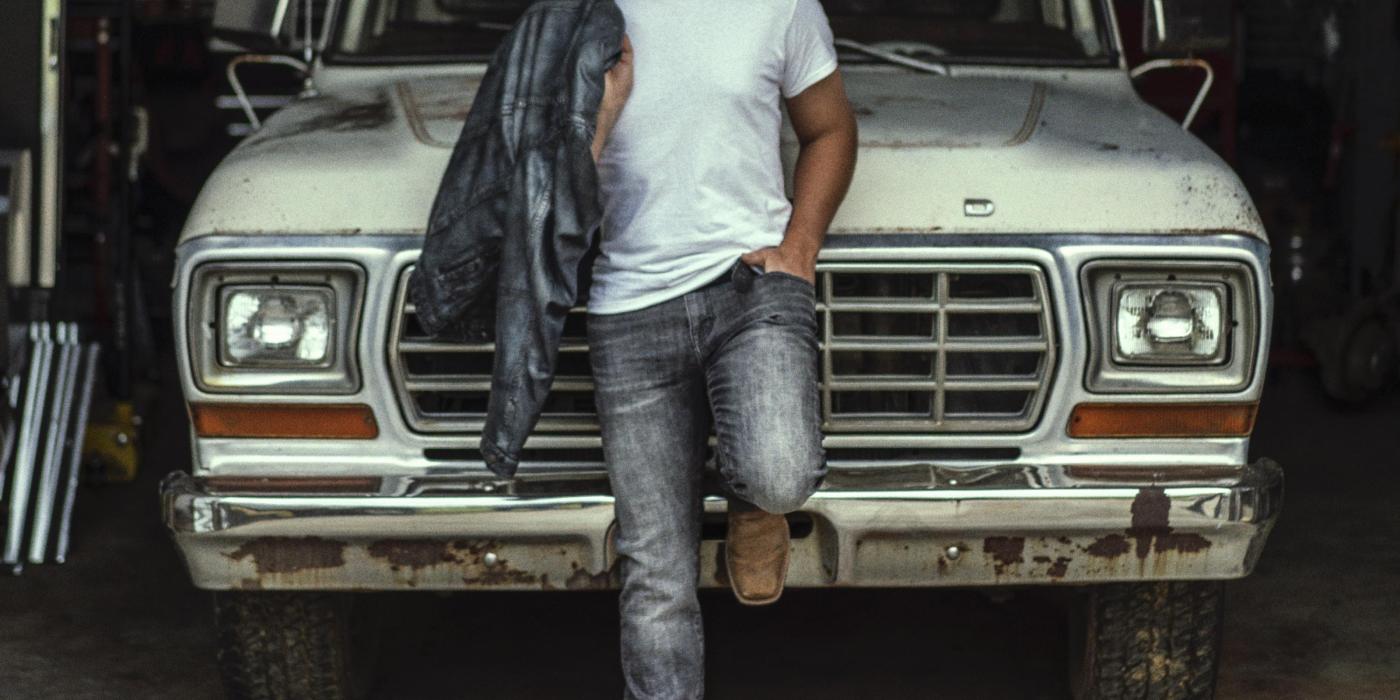 Scotty McCreery leaning back on front of an old truck wearing jeans and t-shirt