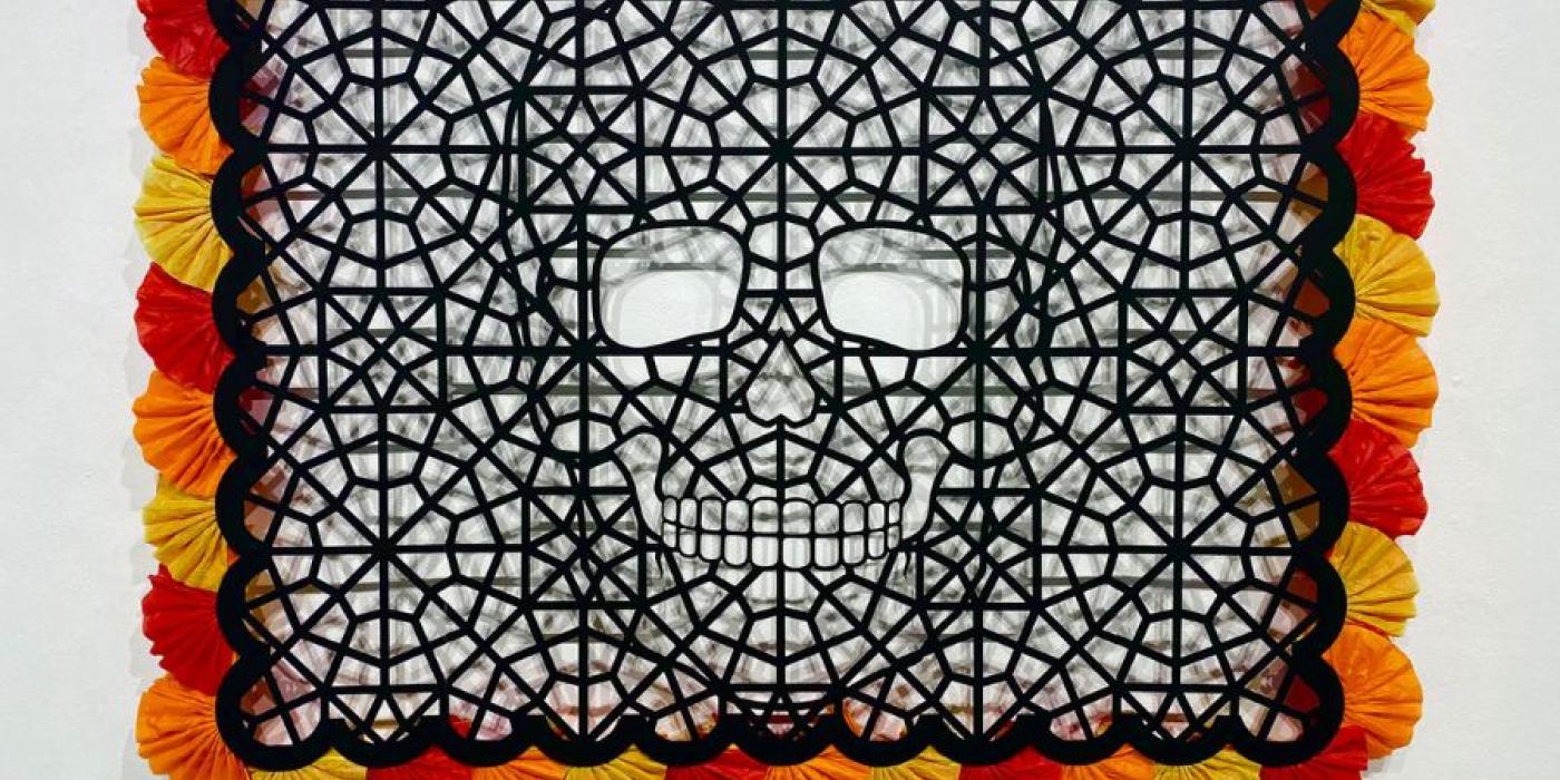 black rectangle with decorative cut outs making up a skeleton head. The black rectangle has red, yellow and orange fluffy decoration around the outside.
