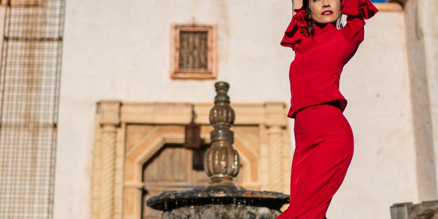 A tall woman poses in front of a mission in a red dress with ruffles at the hem