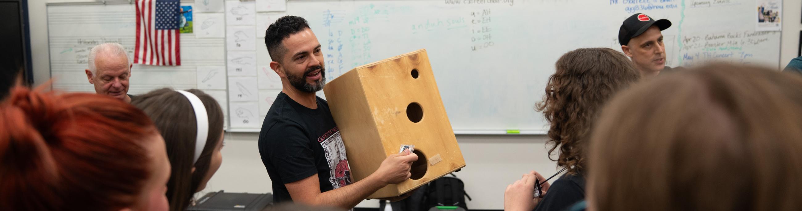 percussionist shows a group of students how to play a cajon