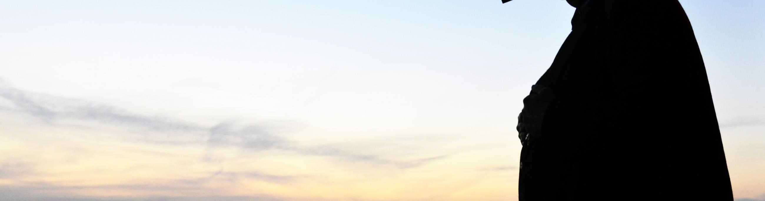 A man stands in silhouette against a sunset over the water