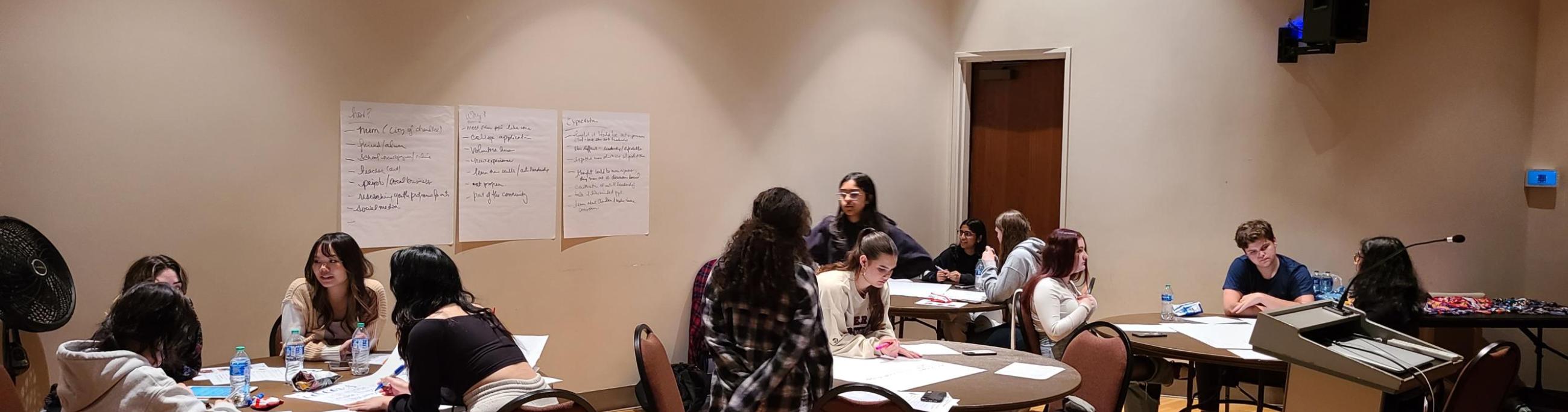 Students work around tables, talking and making notes about a project