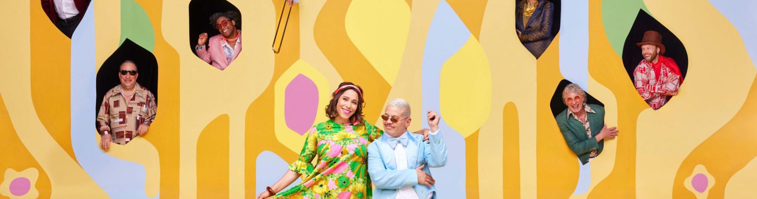 two people standing in front of a yellow background with lots of holes cut out and people sticking their heads out of the holes