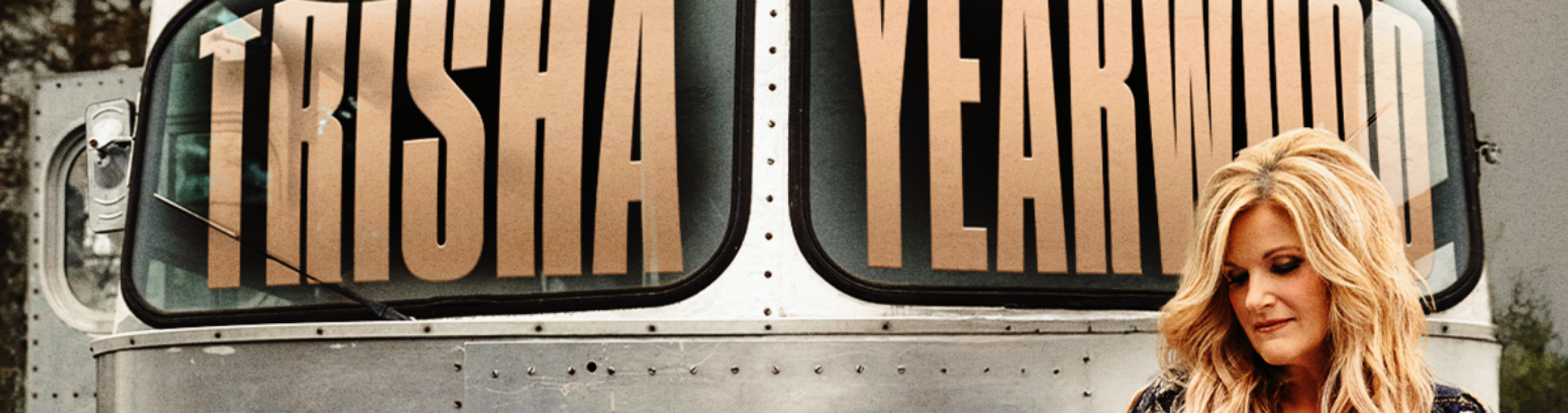 Blonde woman standing in front of silver bus that says Trisha Yearwood