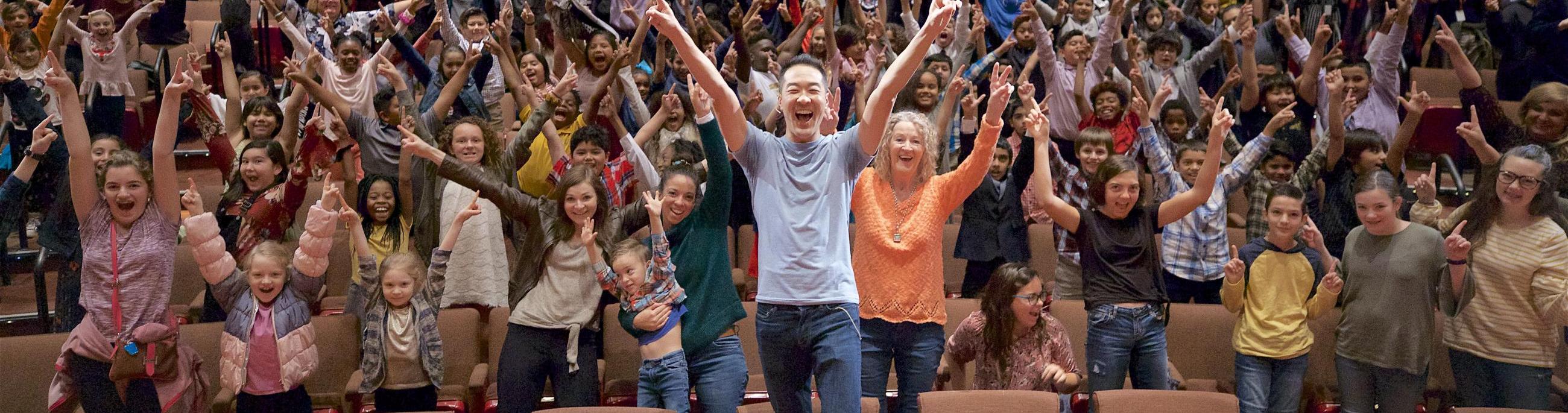 An entire audience of adults and youth are standing up and yelling jubiliantly