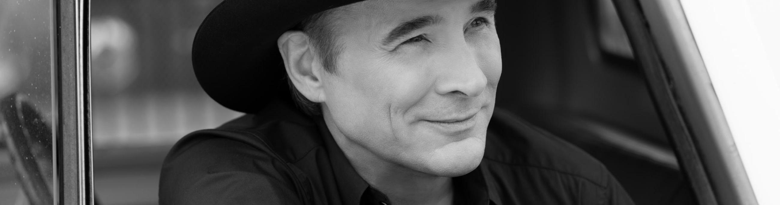 white man with black hat in black and white photo looking outside a car window